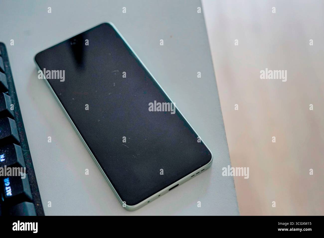 Un elegante smartphone appoggiato su una scrivania accanto alla tastiera di un computer. Il design è minimalista e mostra uno stile di vita tecnologico moderno. Foto Stock