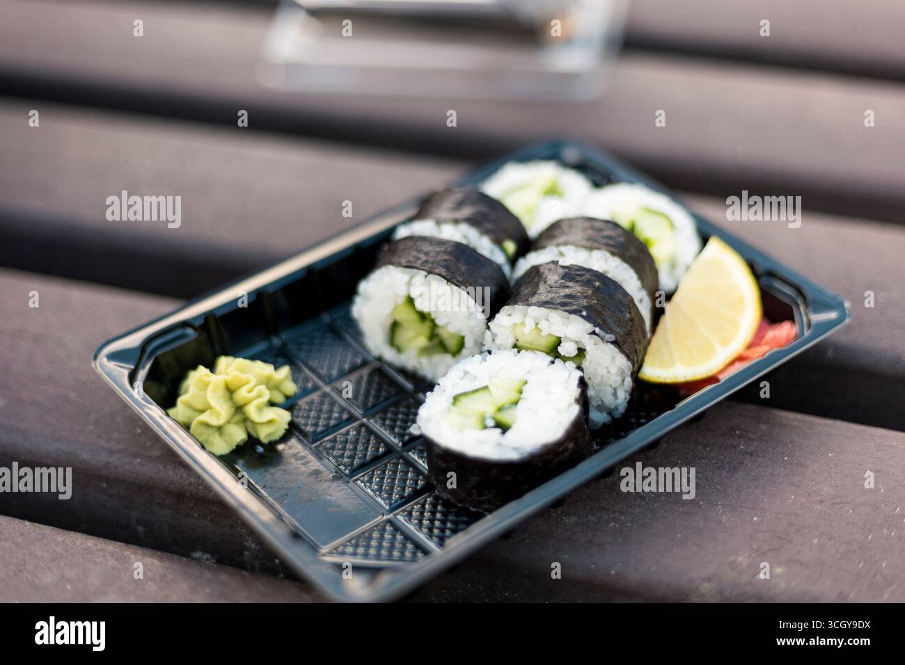 Gli involtini di sushi riempiti di cetriolo sono ordinatamente disposti su un vassoio nero Una bambole di wasabi e una fetta di limone completano i panini, creando un Foto Stock