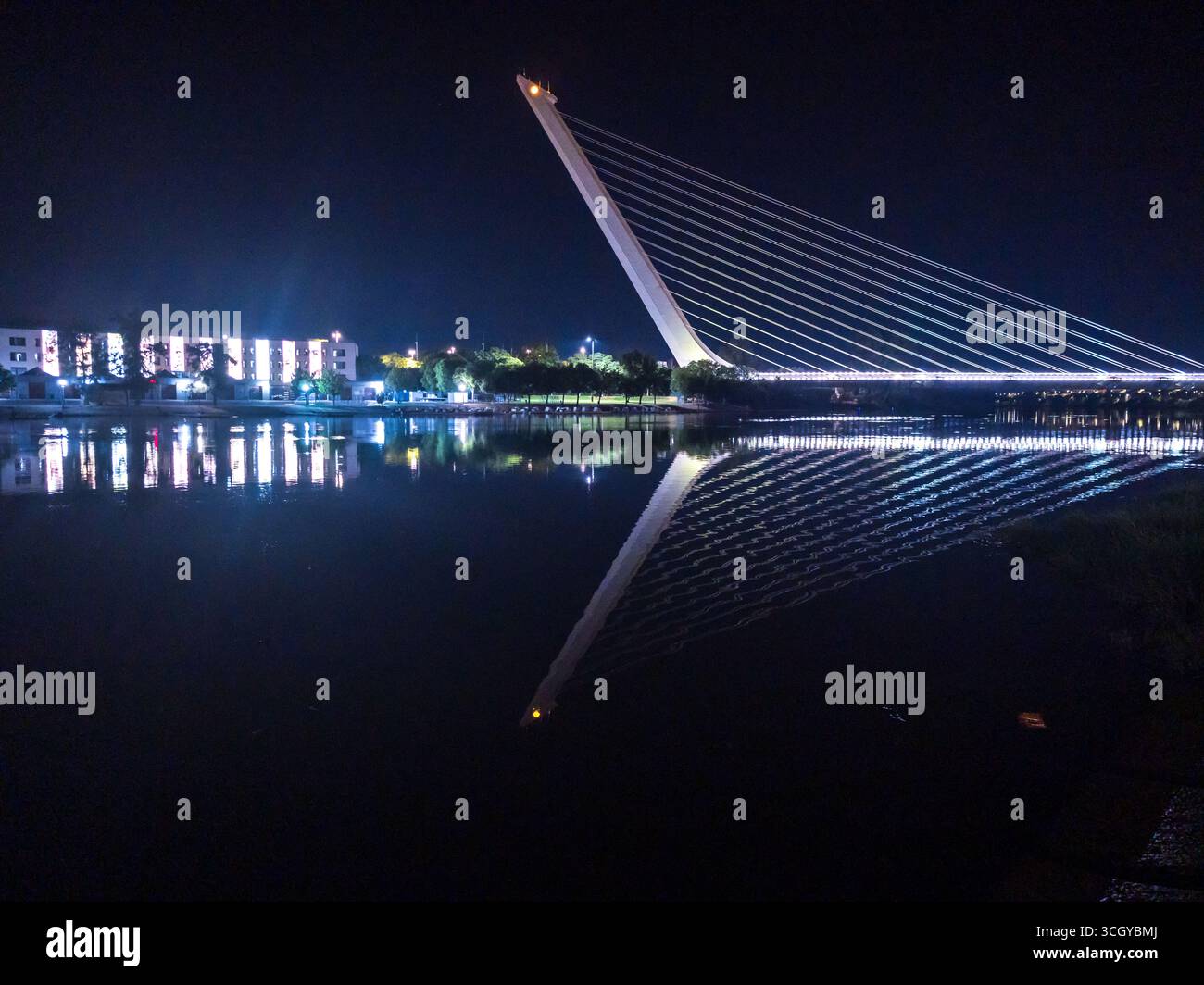 La notte d'estate a Siviglia mostra il ponte Alamillo e l'isola di Cartuja che si riflettono splendidamente sulle acque calme del fiume Guadalquivir. Foto Stock