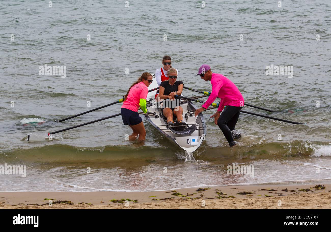 Studland, Dorset Regno Unito. 30 agosto 2025. Il primo giorno dei due giorni di gare del più grande British Rowing Beach Sprint Championships (BRBSC) si svolge a Knoll Beach, Studland, con un numero record di canottieri. Partendo da uno sprint sulla spiaggia per una persona per ogni equipaggio, i vogatori proseguono per 250 m in mare, sfrecciando intorno a due boe, prima di girarne un terzo e tornare direttamente a riva, prima dello sprint finale sulla spiaggia verso un cicalino. Due barche vanno testa a testa in gare con la barca più veloce che progredisce e il secondo posto viene messo fuori combattimento. Crediti: Carolyn Jenkins/Alamy Live News Foto Stock