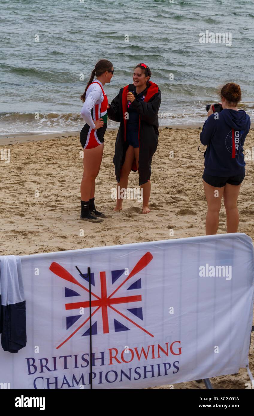 Studland, Dorset Regno Unito. 30 agosto 2025. Il primo giorno dei due giorni di gare del più grande British Rowing Beach Sprint Championships (BRBSC) si svolge a Knoll Beach, Studland, con un numero record di canottieri. Partendo da uno sprint sulla spiaggia per una persona per ogni equipaggio, i vogatori proseguono per 250 m in mare, sfrecciando intorno a due boe, prima di girarne un terzo e tornare direttamente a riva, prima dello sprint finale sulla spiaggia verso un cicalino. Due barche vanno testa a testa in gare con la barca più veloce che progredisce e il secondo posto viene messo fuori combattimento. Crediti: Carolyn Jenkins/Alamy Live News Foto Stock
