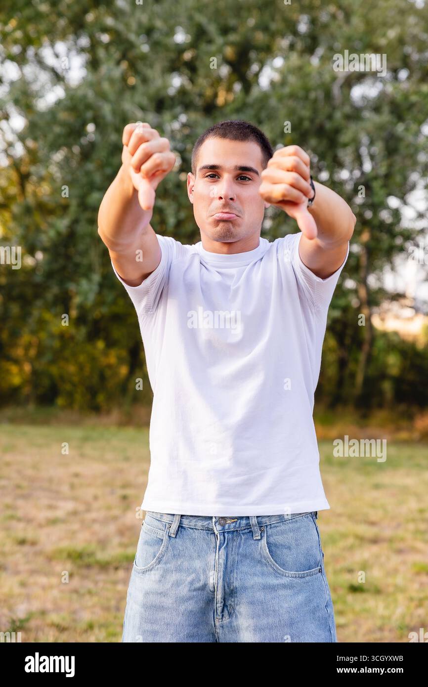 Giovane che mostra un gesto con i pollici in un parco che esprime disapprovazione Foto Stock