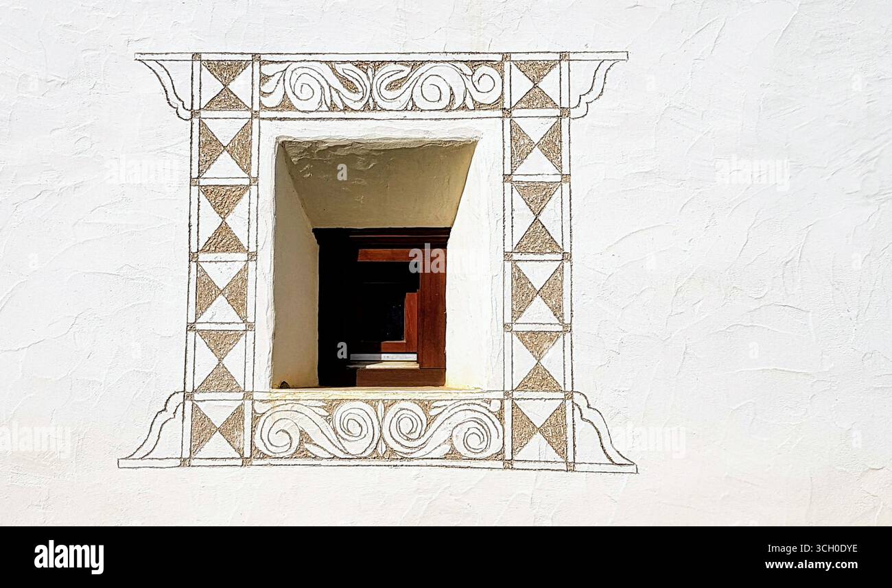 Tipica piccola finestra Engadina con una cornice in legno, bordo decorativo ornamentale e parete bianca intonacata, Svizzera Foto Stock