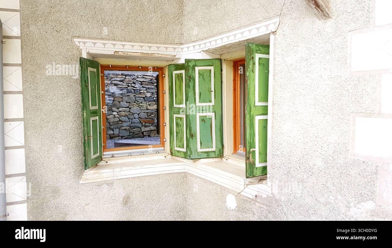 Tipica piccola finestra Engadina con persiane verdi, bordo decorativo oramentale e parete bianca intonacata, Svizzera Foto Stock