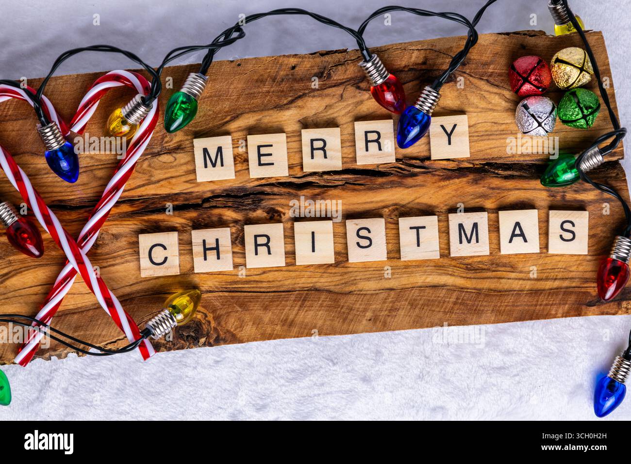 Buon Natale scritto utilizzando piastrelle di lettere di legno su uno sfondo rustico in legno; circondato da colorate luci natalizie; bastoncini di caramelle; e festivi Foto Stock