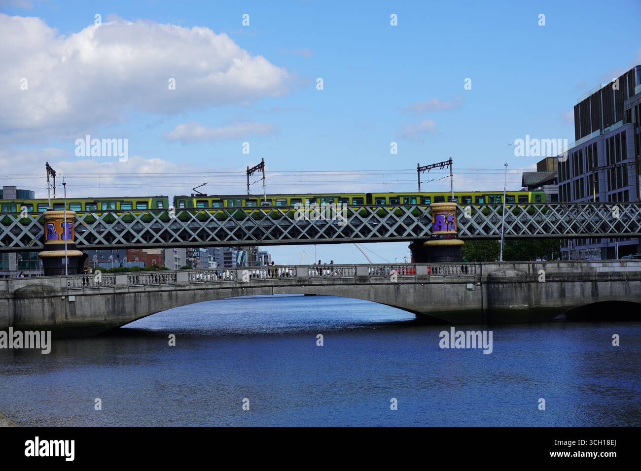 Un treno che attraversa il ponte Loopline sul fiume Liffey a Dublino, con acqua blu e un cielo luminoso come sfondo. Foto Stock