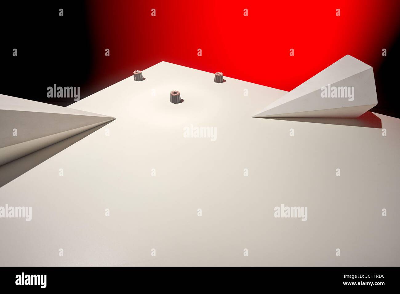 Una foto artistica con una disposizione minimalista di piccole caramelle al cioccolato su una superficie bianca liscia, con strutture angolari astratte e un rosso Foto Stock
