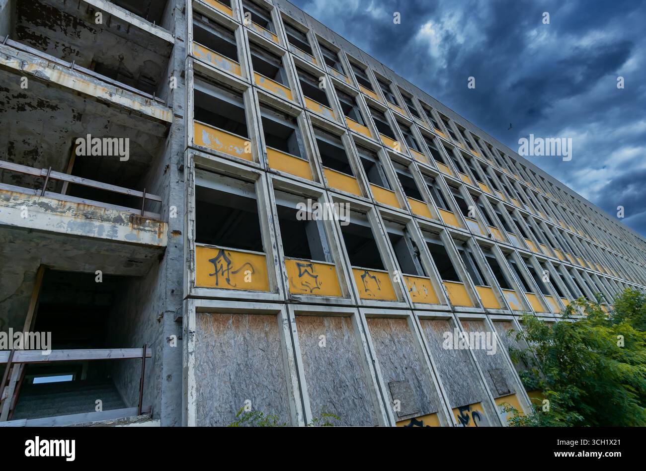 Vista dettagliata della facciata deserta di un edificio a pannelli con elementi gialli, finestre rotte e cielo tempestoso vicino a Berlino. Foto Stock
