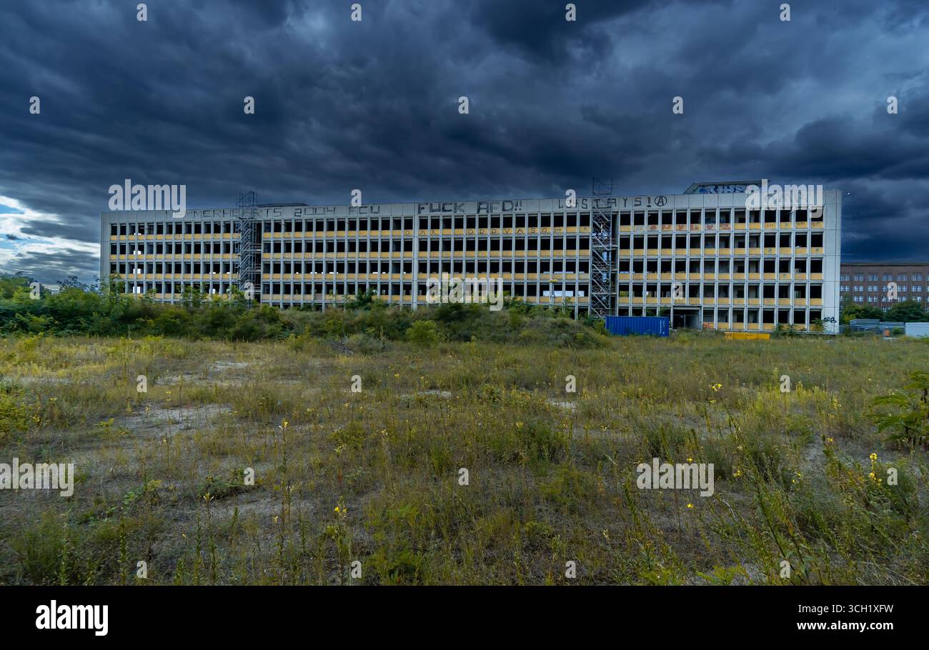 Edificio abbandonato con facciata gialla e graffiti sul tetto nella periferia di Berlino, sotto le spettacolari nuvole di tempesta scure. Foto Stock