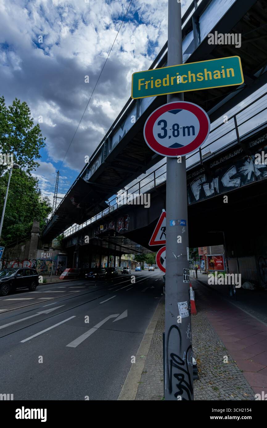 Vista verticale del cartello del quartiere Friedrichshain con il ponte ferroviario e i segnali stradali sulla strada urbana di Berlino. Foto Stock