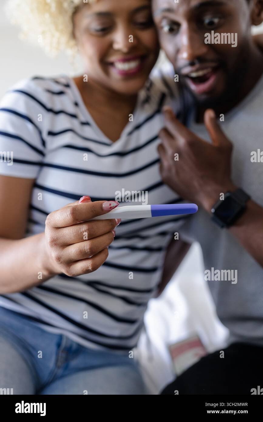 Coppia con gioia che tiene il test di gravidanza, festeggiando le eccitanti notizie a casa Foto Stock