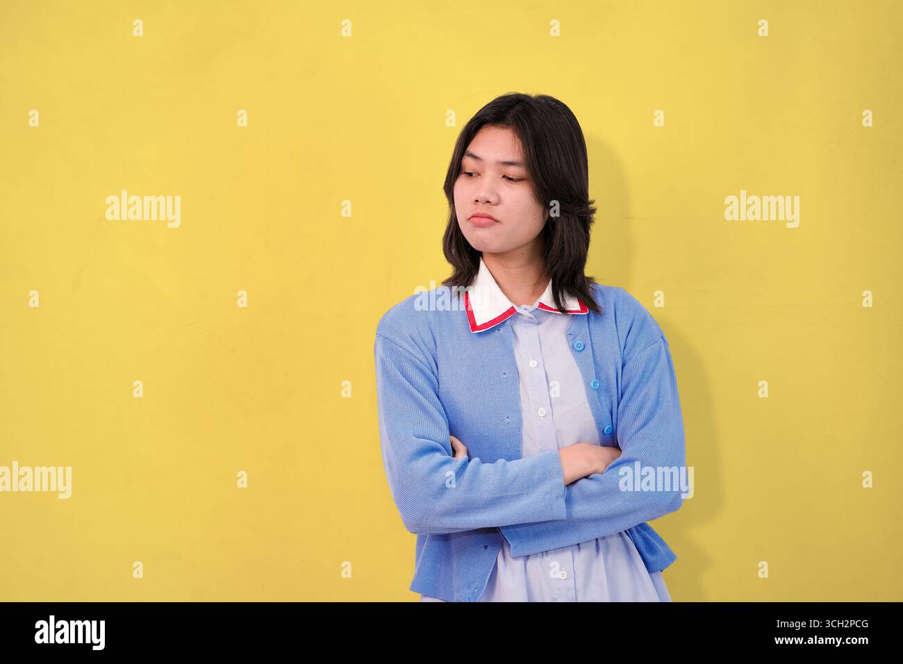 giovane che posa con un maglione blu su uno sfondo giallo brillante Foto Stock