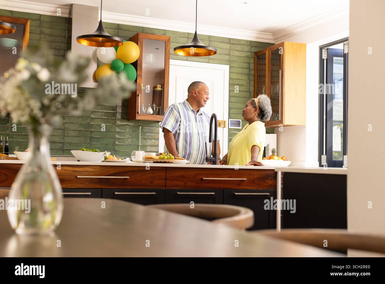 Coppia senior che si diverte a conversare in una cucina moderna con palloncini festivi Foto Stock