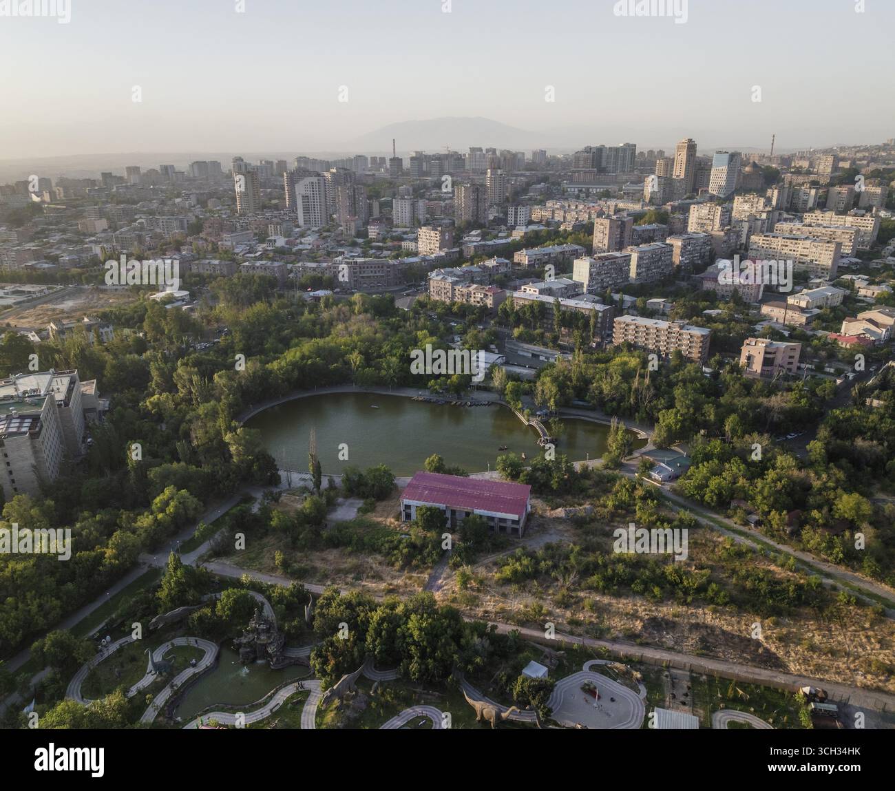 Vista aerea del tranquillo laghetto di un parco cittadino che riflette il cielo, mentre gli edifici moderni si insinuano in lontananza, creando un vibrante contrasto tra natura e urbanità, Erevan, Armenia. Foto Stock
