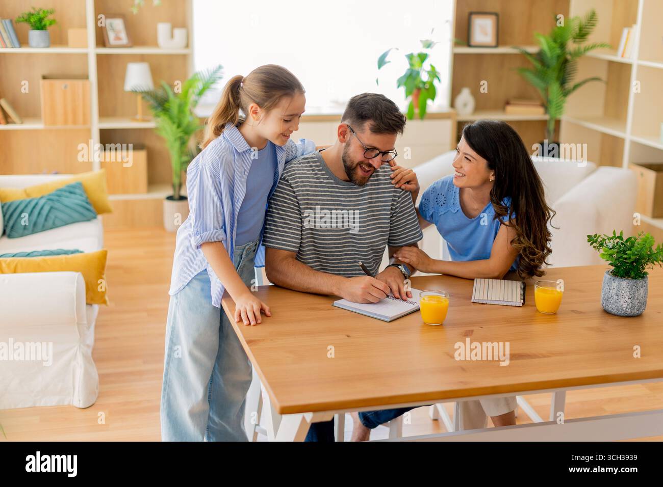 Due bambini condividono momenti di gioia con il padre mentre intraprendono attività creative nella loro accogliente casa durante un pomeriggio di sole. Foto Stock