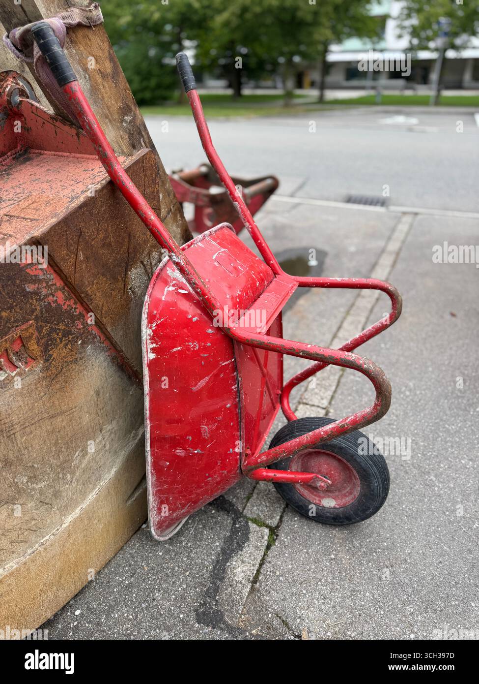 Una carriola rossa è appoggiata contro un muro in un ambiente urbano o in un ambiente frenetico Foto Stock