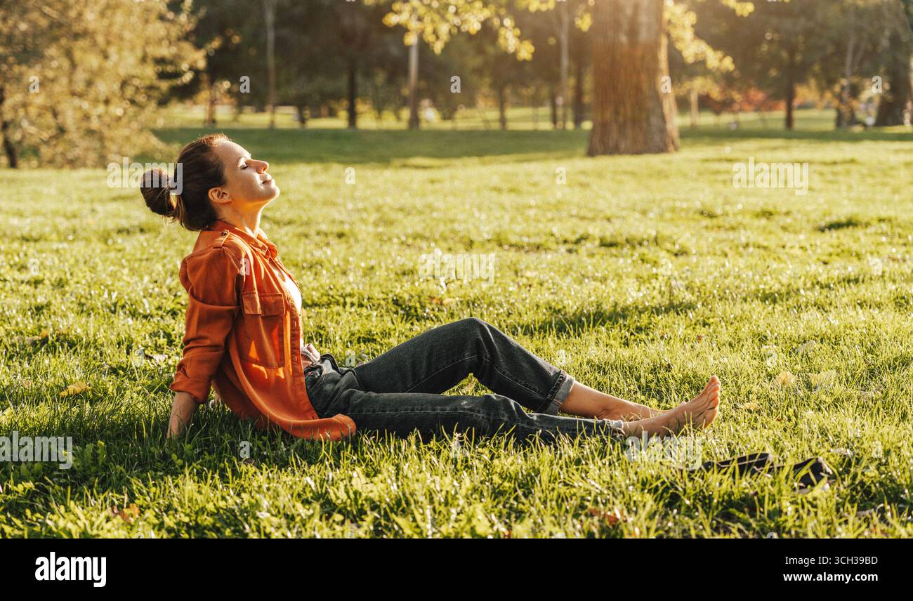 donna a piedi nudi che riposa sull'erba del parco Foto Stock