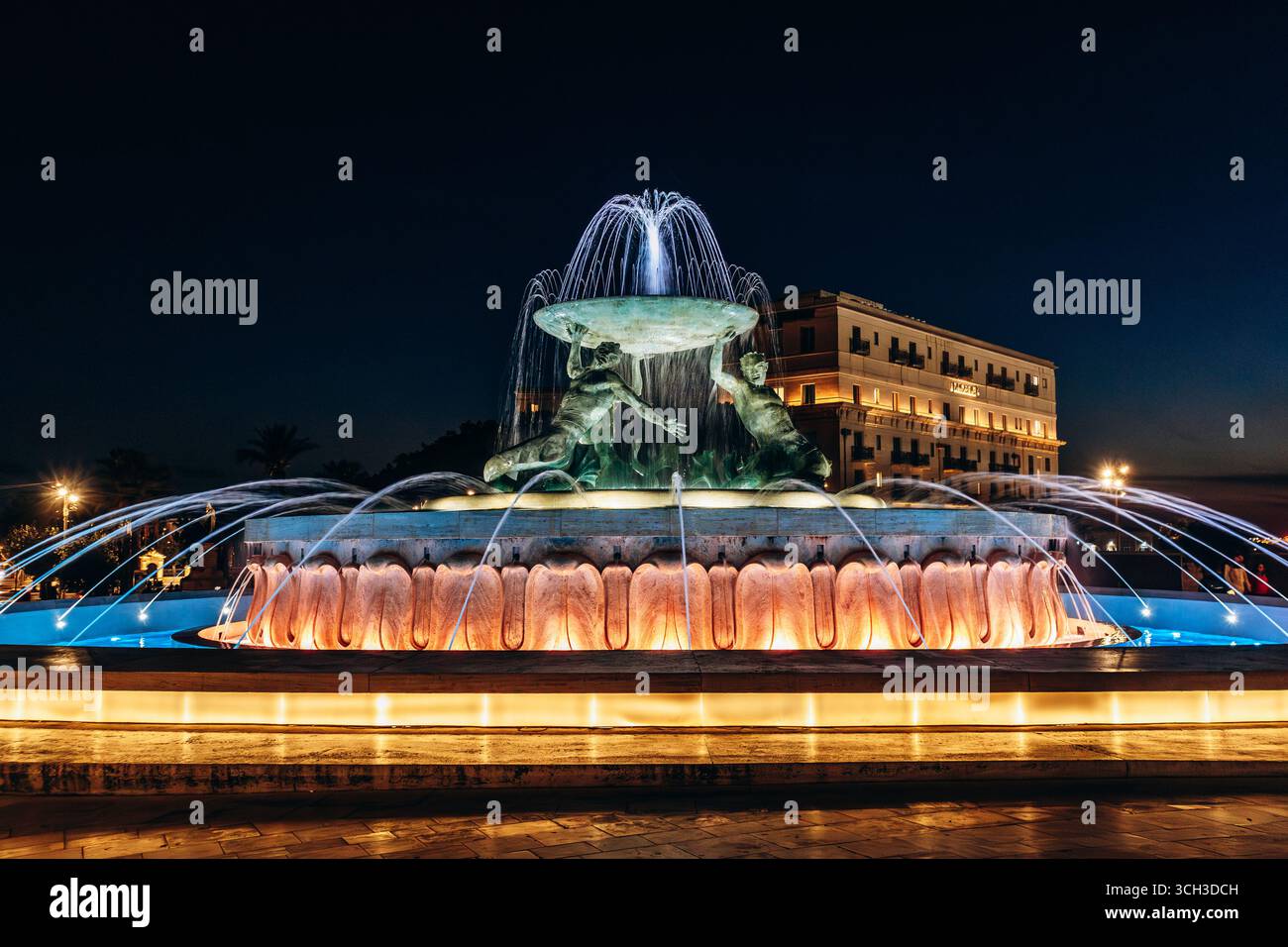 La Fontana del Tritone illuminata di notte, con tre figure di bronzo che tengono in mano un grande bacino all'ingresso della città di la Valletta Foto Stock