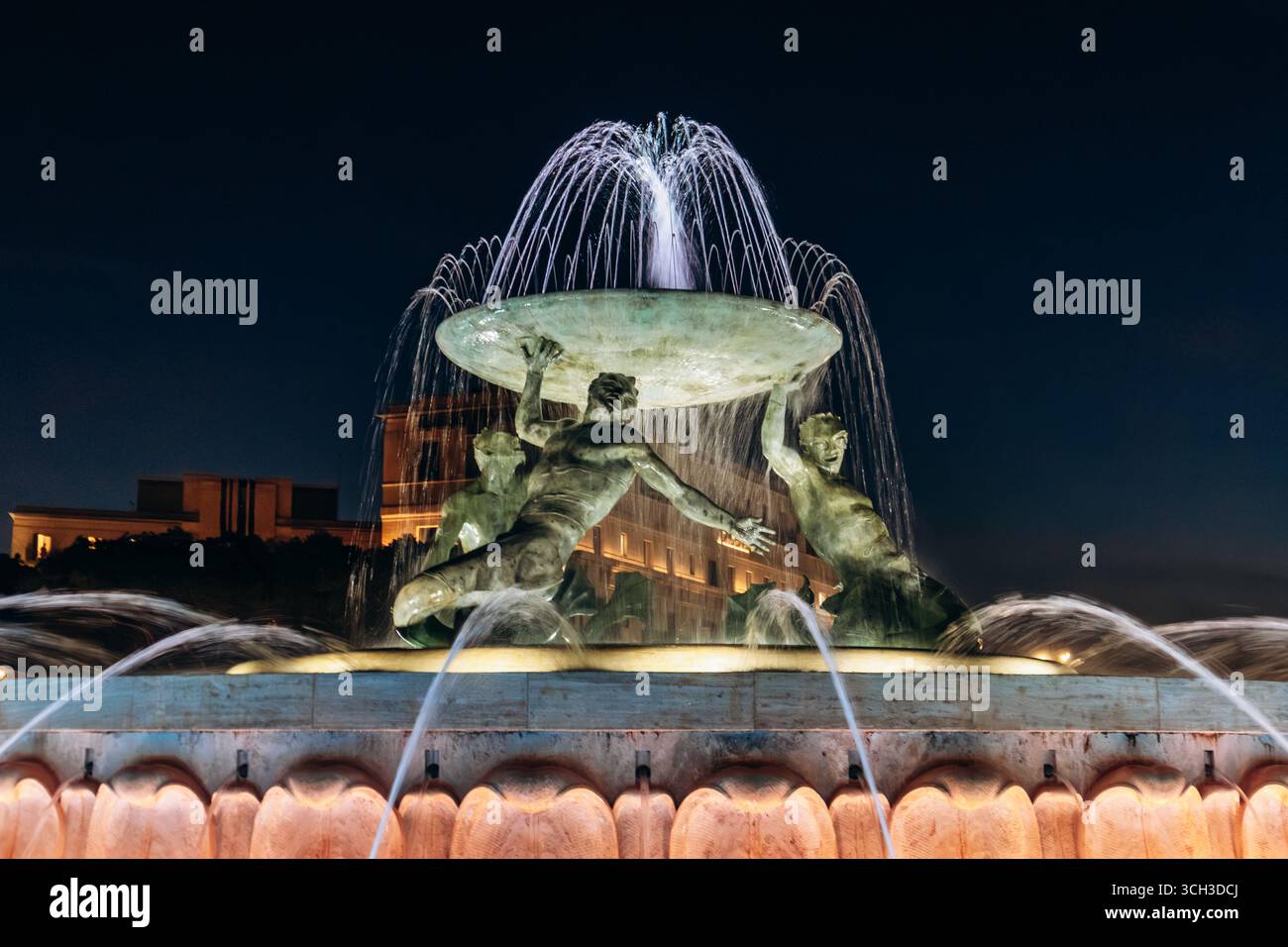 La Fontana del Tritone illuminata di notte, con tre figure di bronzo che tengono in mano un grande bacino all'ingresso della città di la Valletta Foto Stock