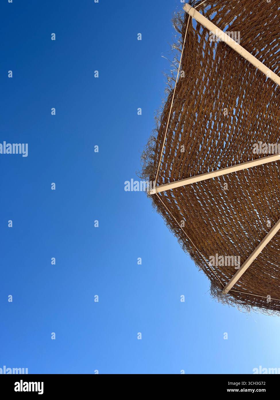 Ombrellone di paglia contro un cielo azzurro limpido in Algarve, Portogallo. - Immagine stock catturata con smartphone
