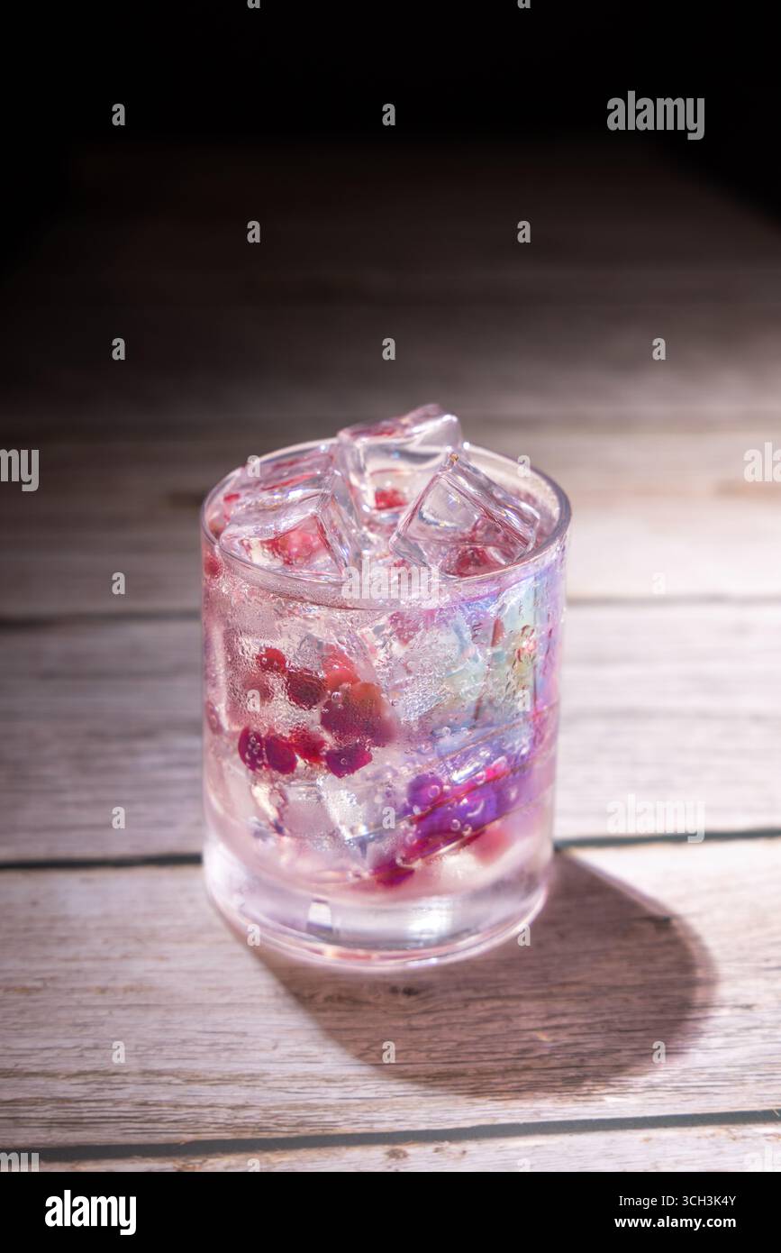 Gin cocktail con semi di melograno e cubetti di ghiaccio in vetro trasparente su una superficie in legno. Bevanda rinfrescante studiata per fotografare bevande gourmet. Foto Stock Gin cocktail con semi di melograno e cubetti di ghiaccio in vetro trasparente su una superficie in legno. Bevanda rinfrescante studiata per fotografare bevande gourmet. Foto Stock