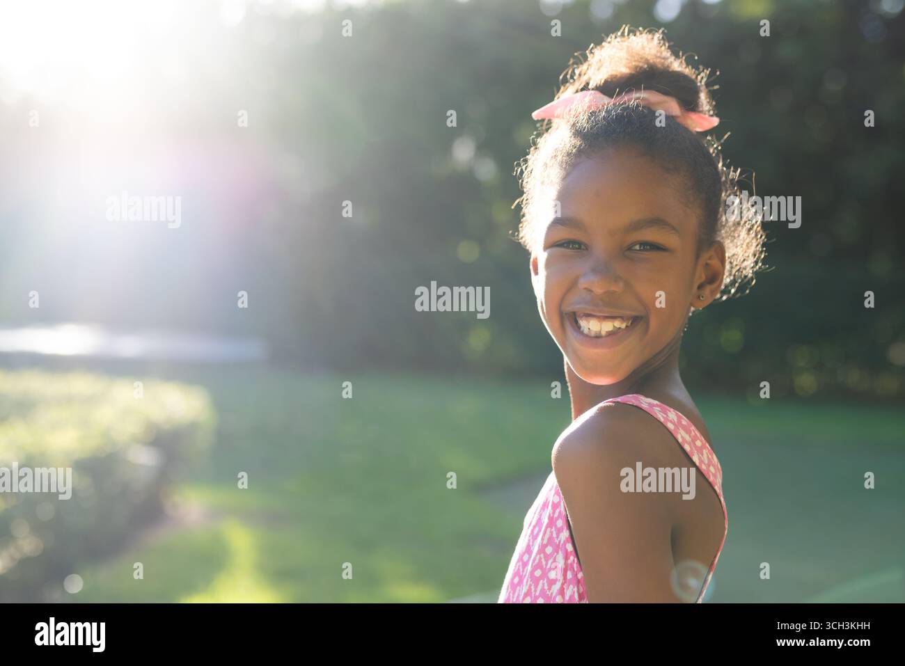 Ragazza sorridente che si gode una giornata di sole in giardino, indossa un abito rosa con fiocco, copia spazio Foto Stock