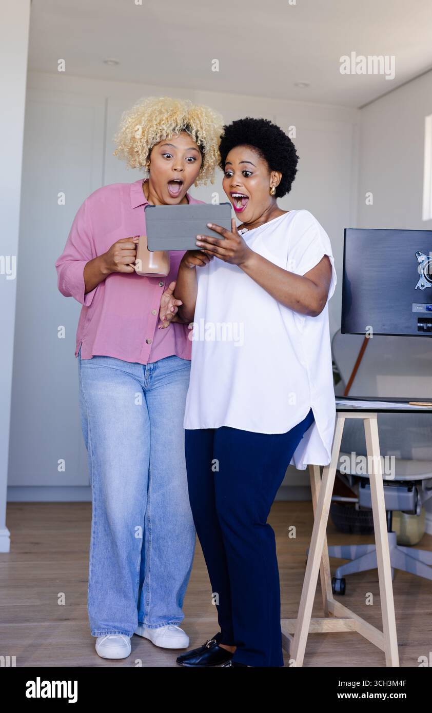 Amici che guardano con entusiasmo lo schermo di un tablet a casa, condividendo una piacevole sorpresa insieme Foto Stock