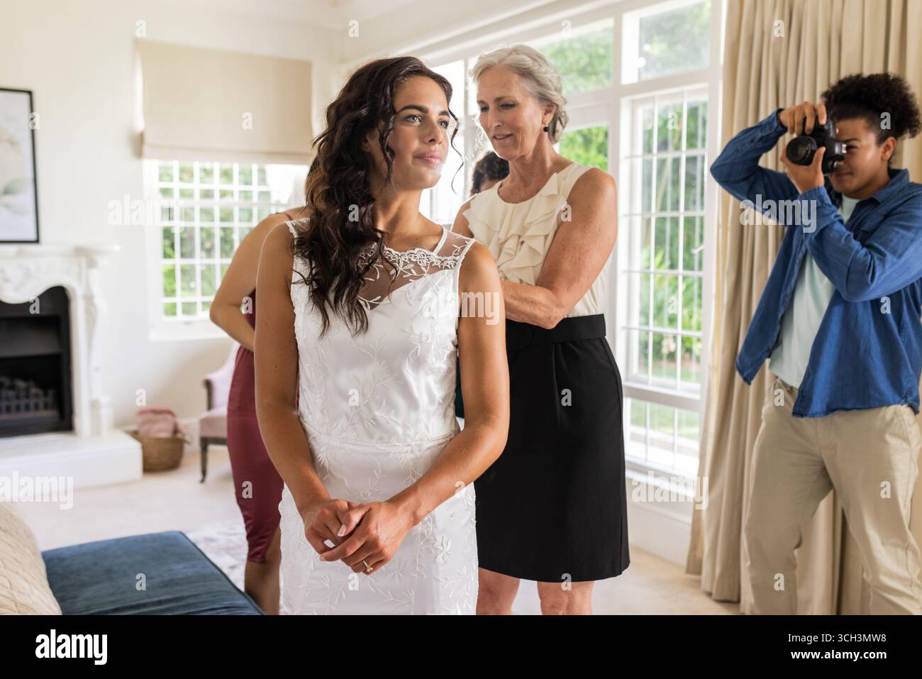 Regolazione dell'abito della sposa, aiuto dei membri della famiglia mentre il fotografo cattura momenti di gioia Foto Stock