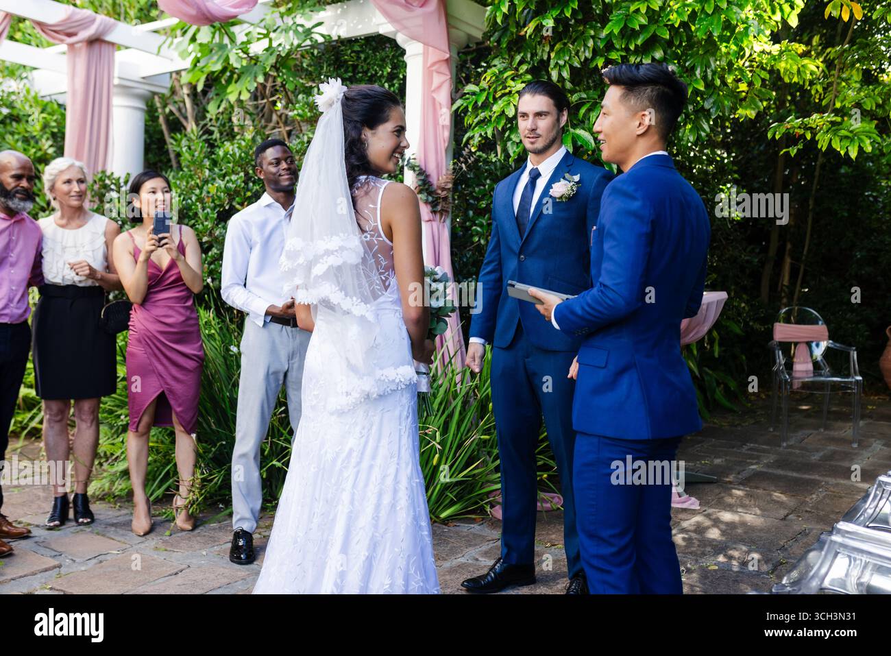 Sposa e sposo si scambiano le promesse all'aperto, circondati da amici e familiari gioiosi Foto Stock