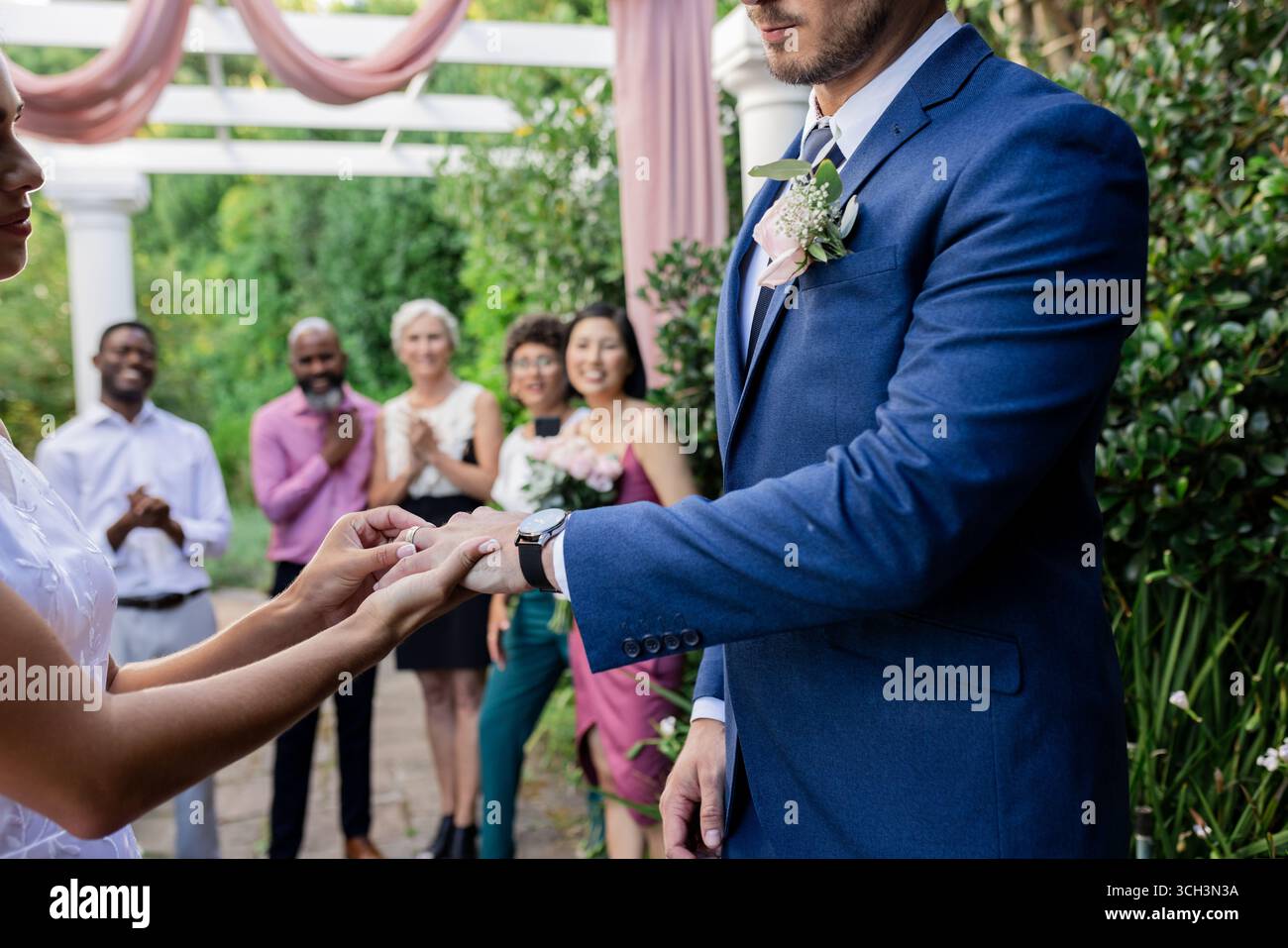 Scambiarsi le fedi durante la cerimonia di nozze all'aperto, circondati da gioiosi amici Foto Stock