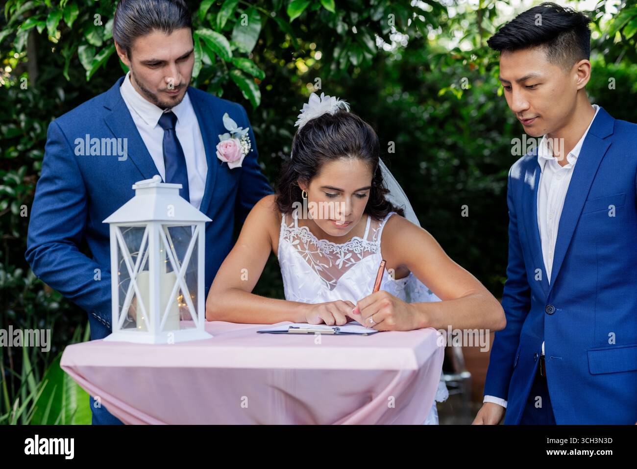La sposa firma un documento di matrimonio all'aperto con lo sposo e l'uomo migliore che guarda Foto Stock