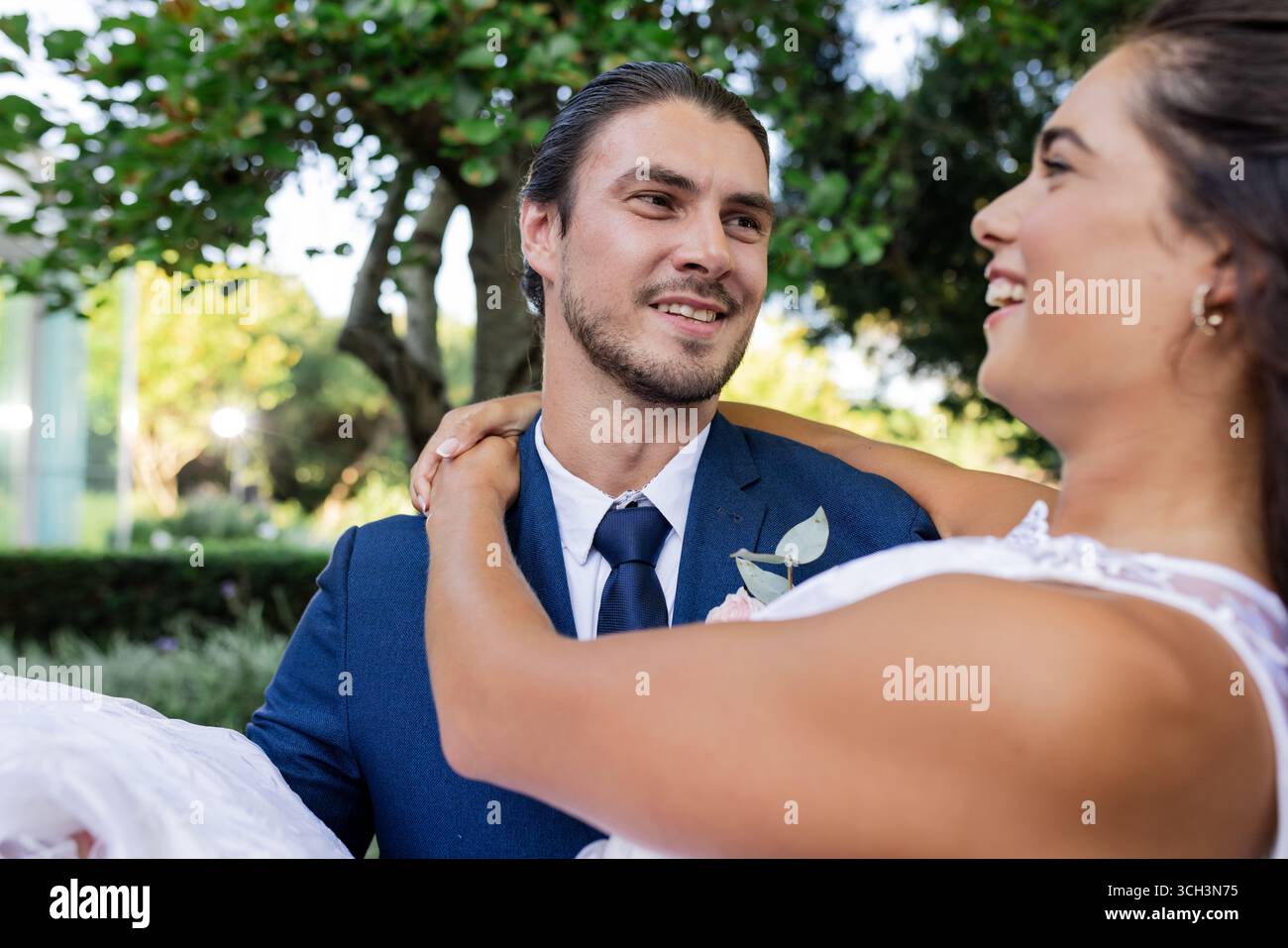Sposo in tuta blu per portare la sposa all'aperto, sorridendo e festeggiando Foto Stock