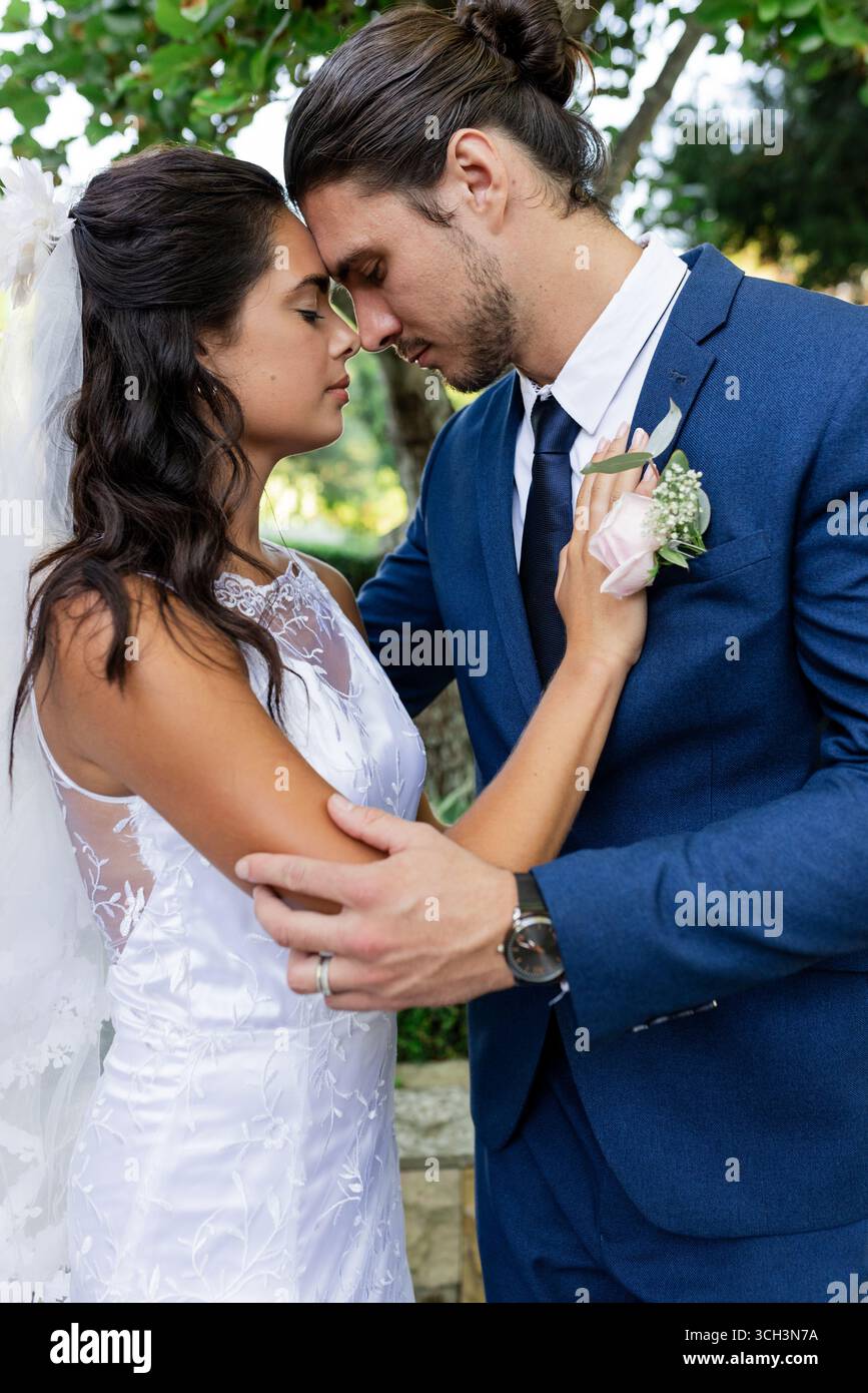 Gli sposi si abbracciano teneramente in giardino, condividendo momenti intimi il giorno del matrimonio Foto Stock