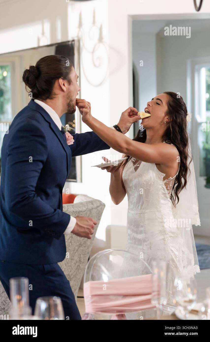 Sposa e sposo si nutrono gioiosamente a vicenda della torta al ricevimento di nozze Foto Stock