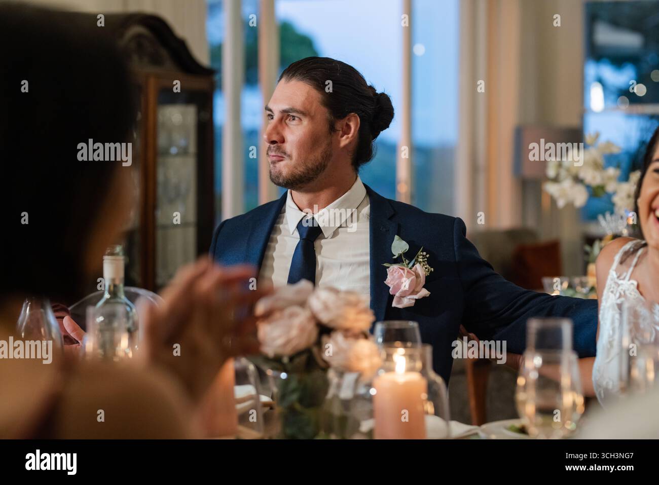Sposo in costume sorridente al tavolo della cena durante le celebrazioni nuziali al chiuso Foto Stock