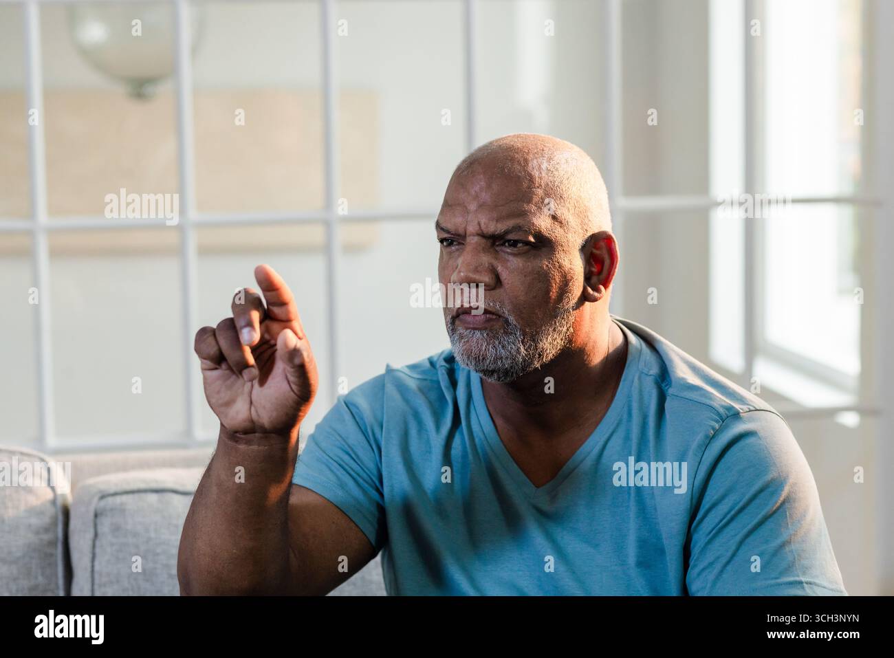 Uomo afroamericano in camicia blu che gestiva mentre era seduto sul divano a casa Foto Stock