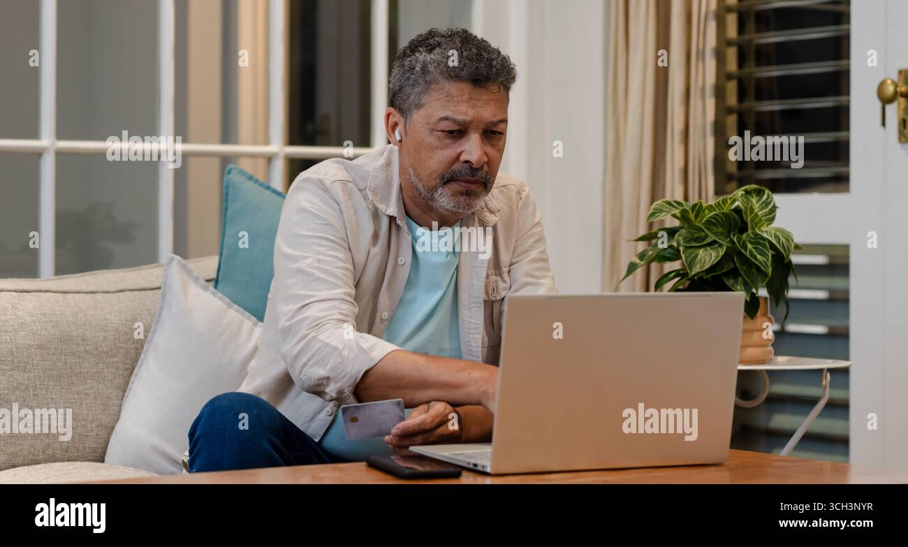 Anziano che usa un computer portatile e tiene in mano la carta di credito a casa, fa shopping online Foto Stock
