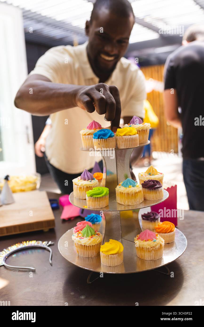 Alla festa, l'uomo organizza cupcake colorati su uno stand a più piani per una felice riunione di famiglia Foto Stock
