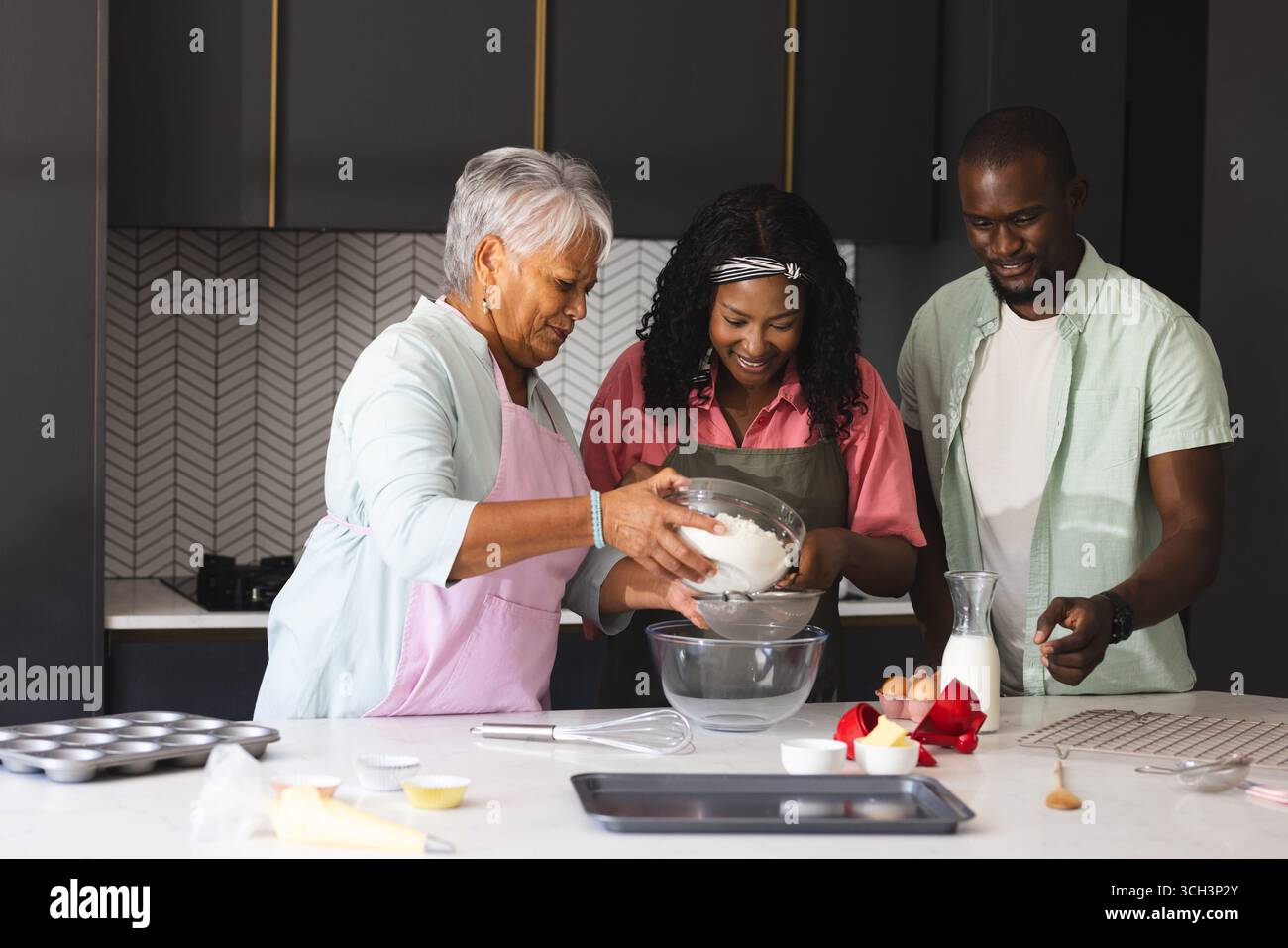Tre generazioni felici cucinano in cucina, condividendo gioia e tradizioni familiari felici, a casa Foto Stock
