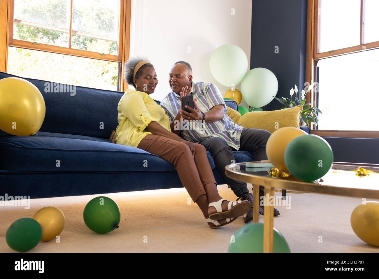 Coppia afroamericana seduto sul divano, sorridente e guardando lo smartphone Foto Stock