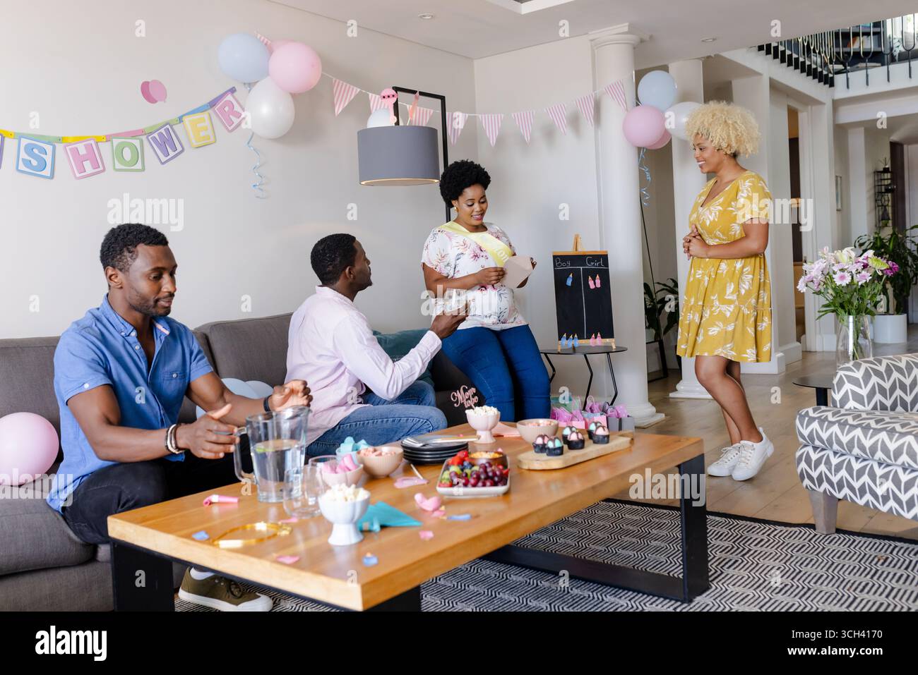 Gli amici festeggiano la baby shower a casa, gustando spuntini e chiacchierando insieme Foto Stock