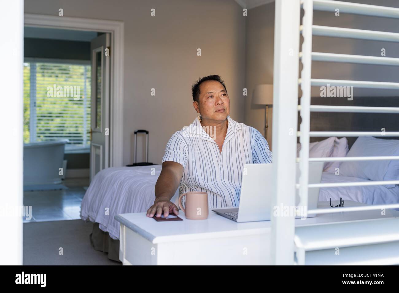 Uomo anziano che lavora su un notebook a casa, si gusta un caffè e ha un aspetto premuroso Foto Stock