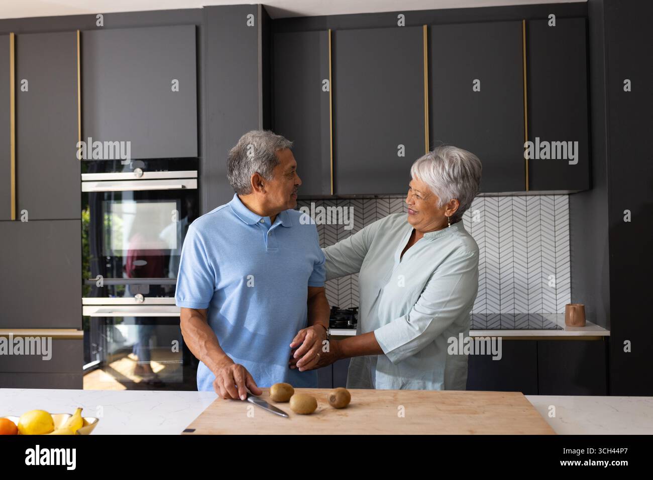 La coppia senior prepara il pasto insieme in una cucina moderna, condividendo momenti di gioia Foto Stock