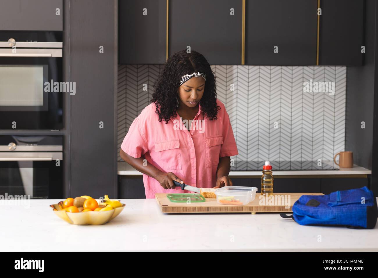 Donna in cucina che prepara il pranzo, affetta il pane sul tagliere, si concentra sul lavoro, a casa Foto Stock
