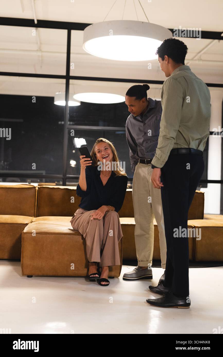 In un ufficio moderno, donna che mostra lo smartphone mentre discute idee con i professionisti Foto Stock