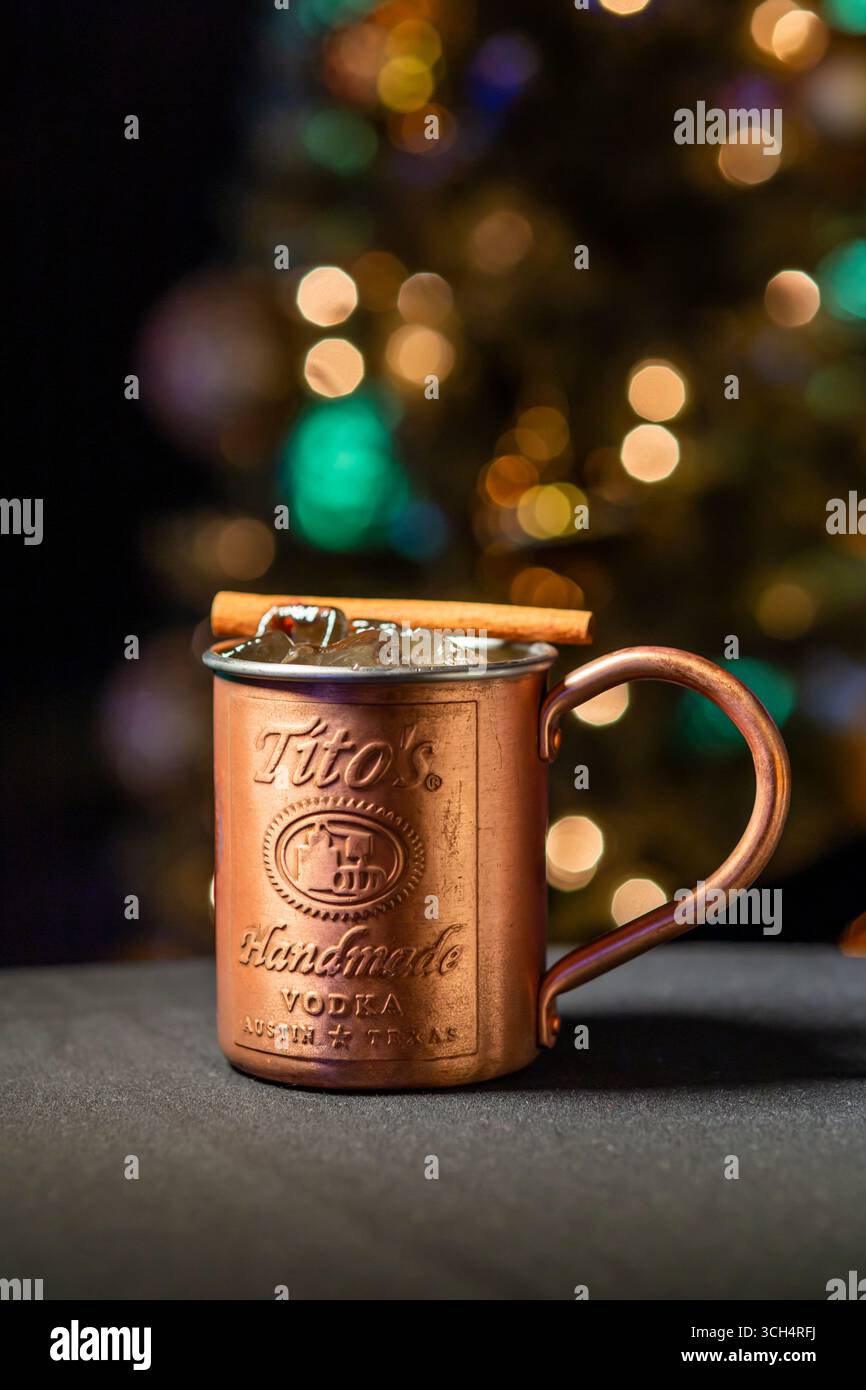Cocktail natalizio servito in una tazza di rame di Tito's Handmade Vodka con ghiaccio e una guarnizione di cannella, adagiata su un caldo sfondo natalizio Foto Stock