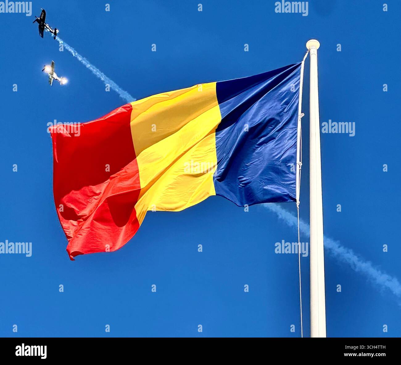 Un Alpha Jet dell'aeronautica francese in livrea blu, bianca e rossa è parcheggiato su un asfalto, con una persona in tuta di volo che cammina nelle vicinanze e negli edifici urbani. Foto Stock