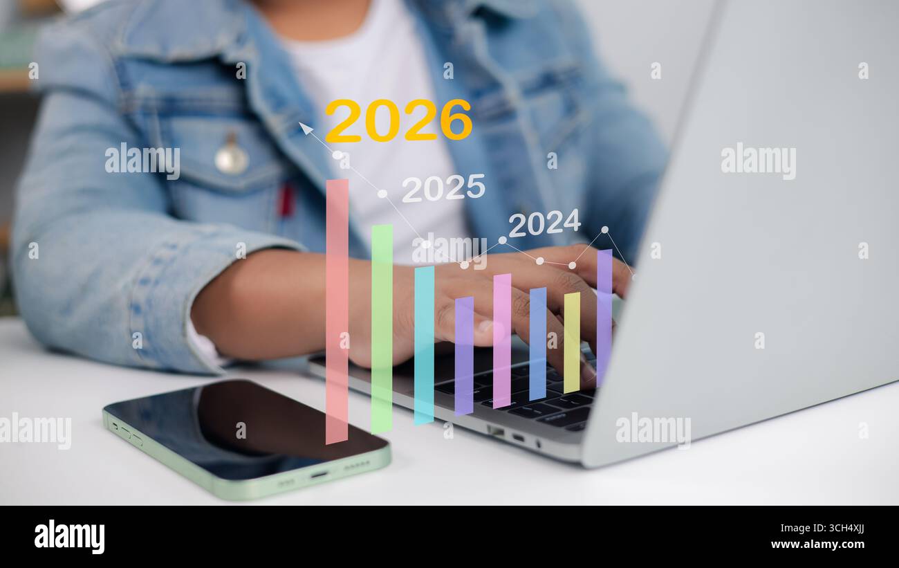 Persona che utilizza un notebook con grafico a barre colorato e grafico a linee che mostra la crescita aziendale dal 2024 al 2026, ideale per previsioni finanziarie, pianificazione e c Foto Stock