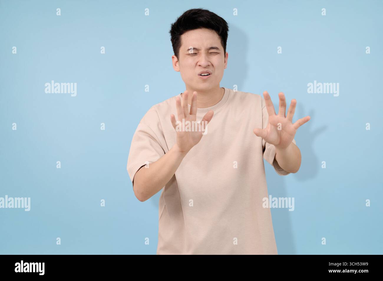 Un uomo gesta con le mani che implicano irritazione o rigetto, posato su uno sfondo blu neutro Foto Stock