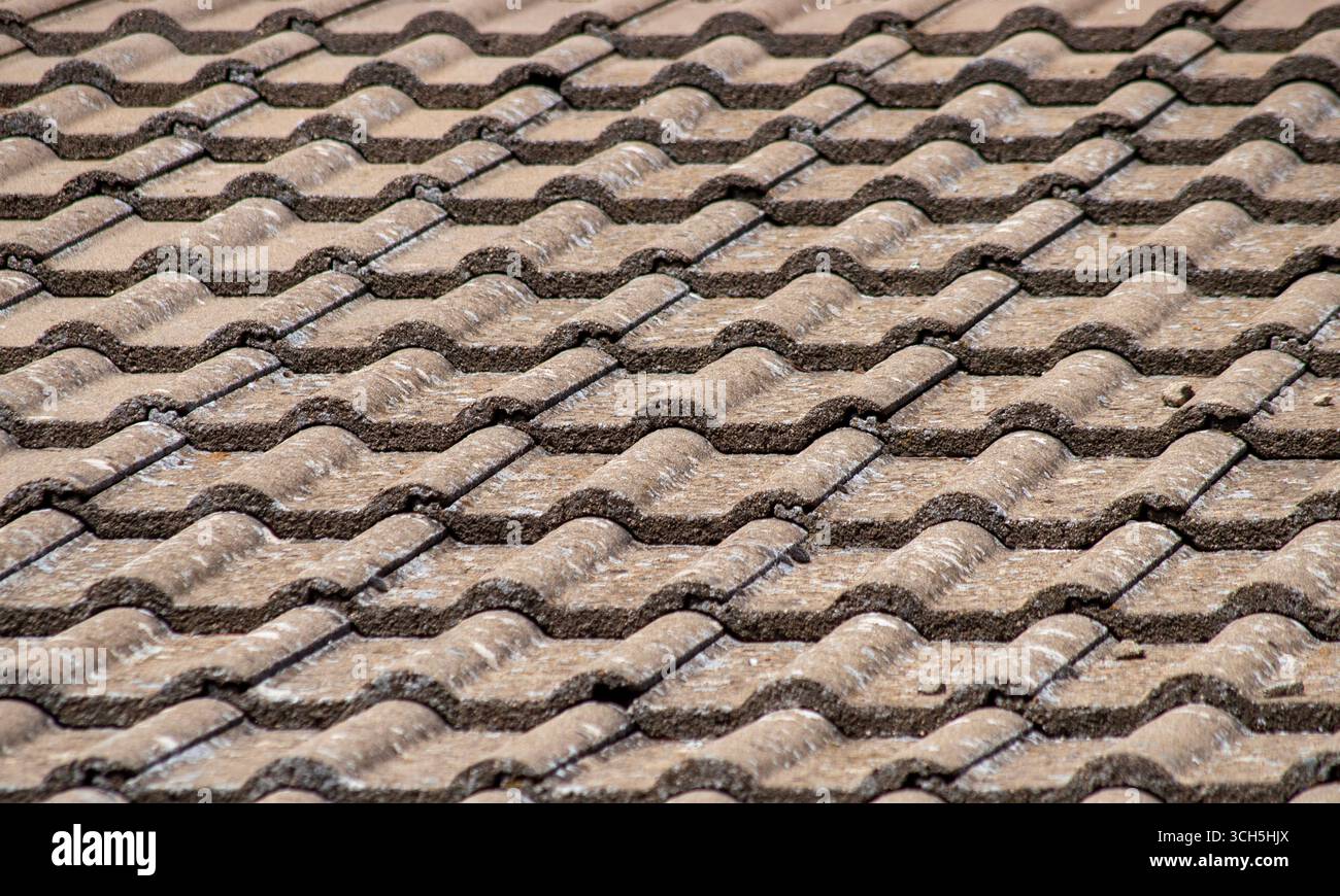 Vista ravvicinata di una texture a motivo di tegola di cemento ondulata. Fondo a file di tegole in argilla marrone sul tetto di un edificio residenziale Foto Stock